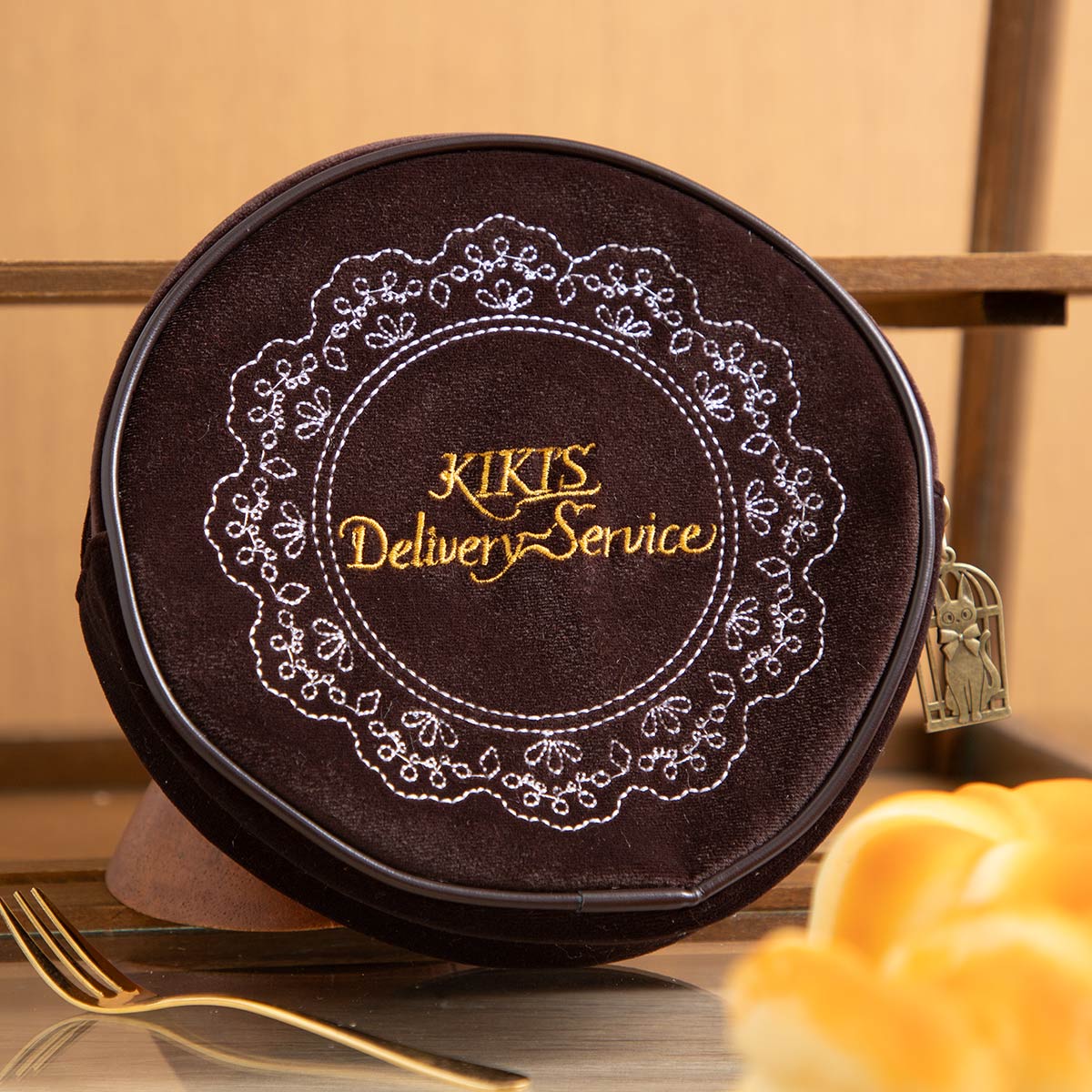 Reverse of the Kiki's Delivery Service pouch with gold script and embroidered cake doily