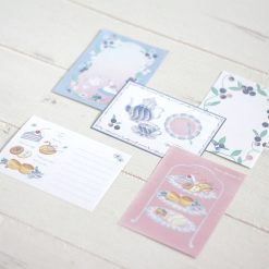 Illustrated Papier Platz Otegaru memo sheets laid out on a white wooden surface, featuring swans, blueberries, desserts, and soft pastel decorative frames.
