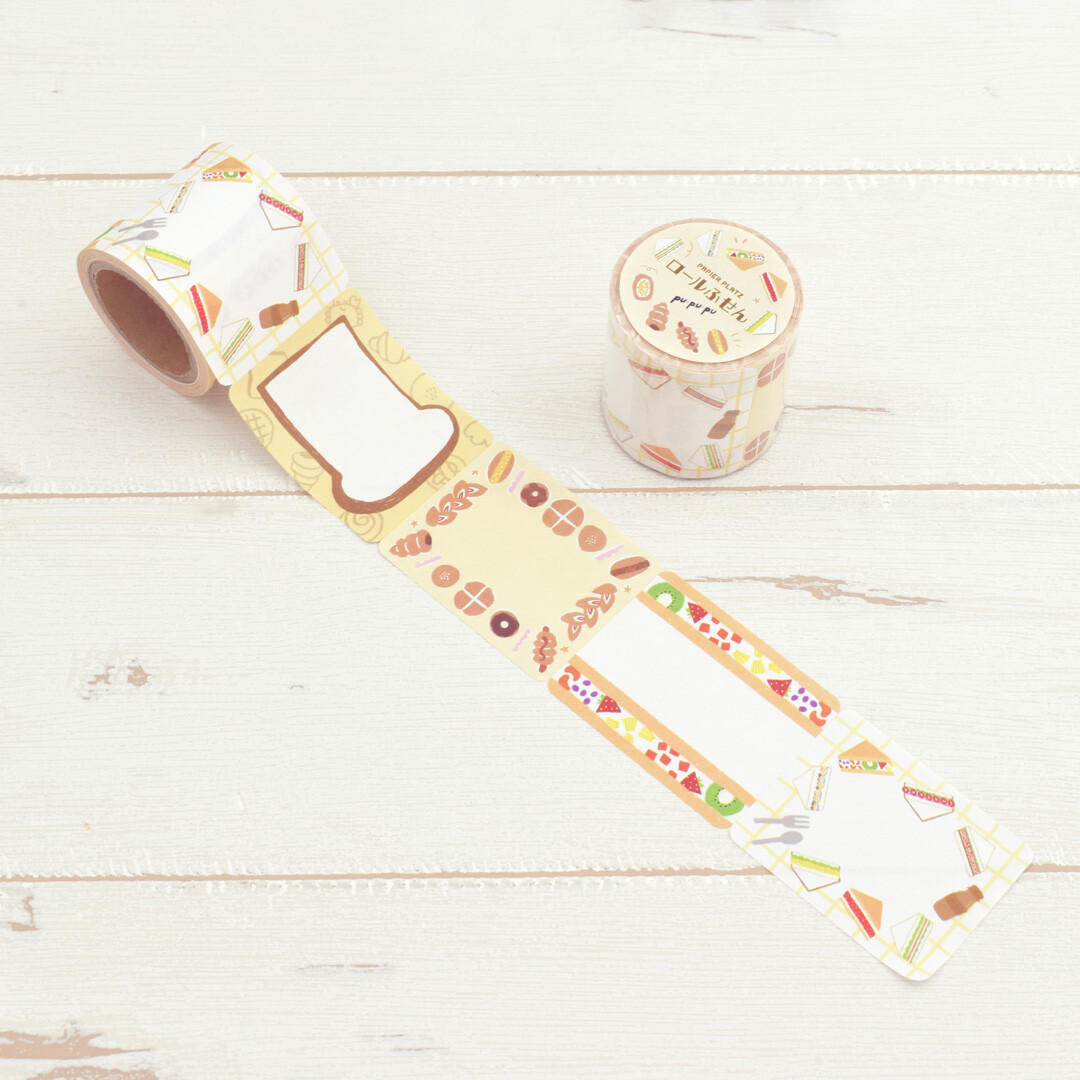 Papier Platz PuPuPu sticky roll labels with sandwich and pastry illustrations, roll partially unwrapped on wooden background.