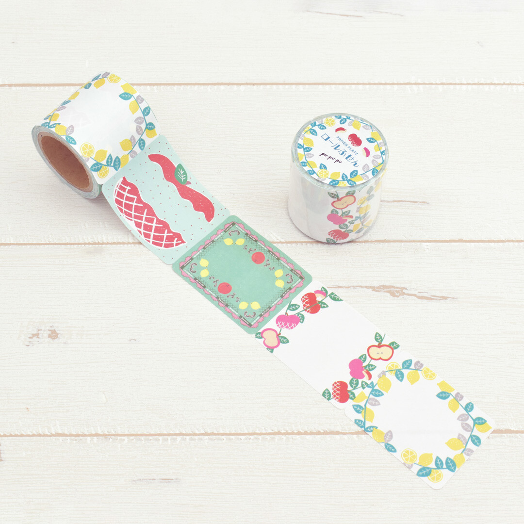 Papier Platz PuPuPu sticky roll with fruit wreath and pastry-themed labels, roll extended and product jar shown on wooden surface.