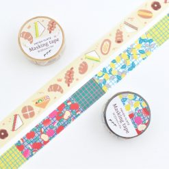 Two Papier Platz Pupupu washi tape designs displayed together, one with bakery-themed illustrations and one with fruit and grid patterns, both shown unrolled with their labelled rolls.