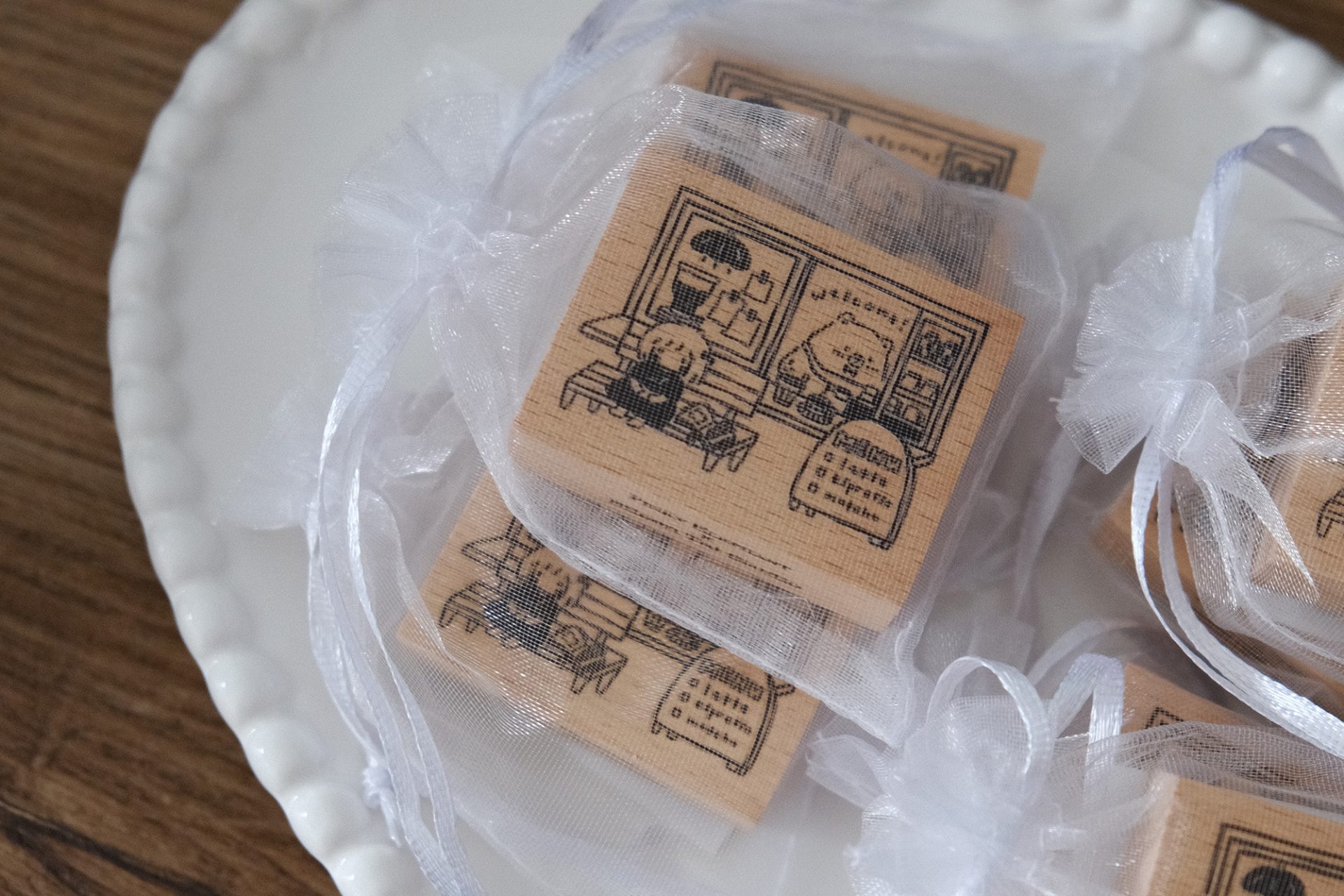 Styled photo of multiple Eileen Tai “Bearista Café Daydream” rubber stamps packaged in organza bags arranged on a plate.