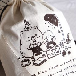 Angled view of an Eileen Tai brown drawstring pouch with character illustration and drawstring closure.