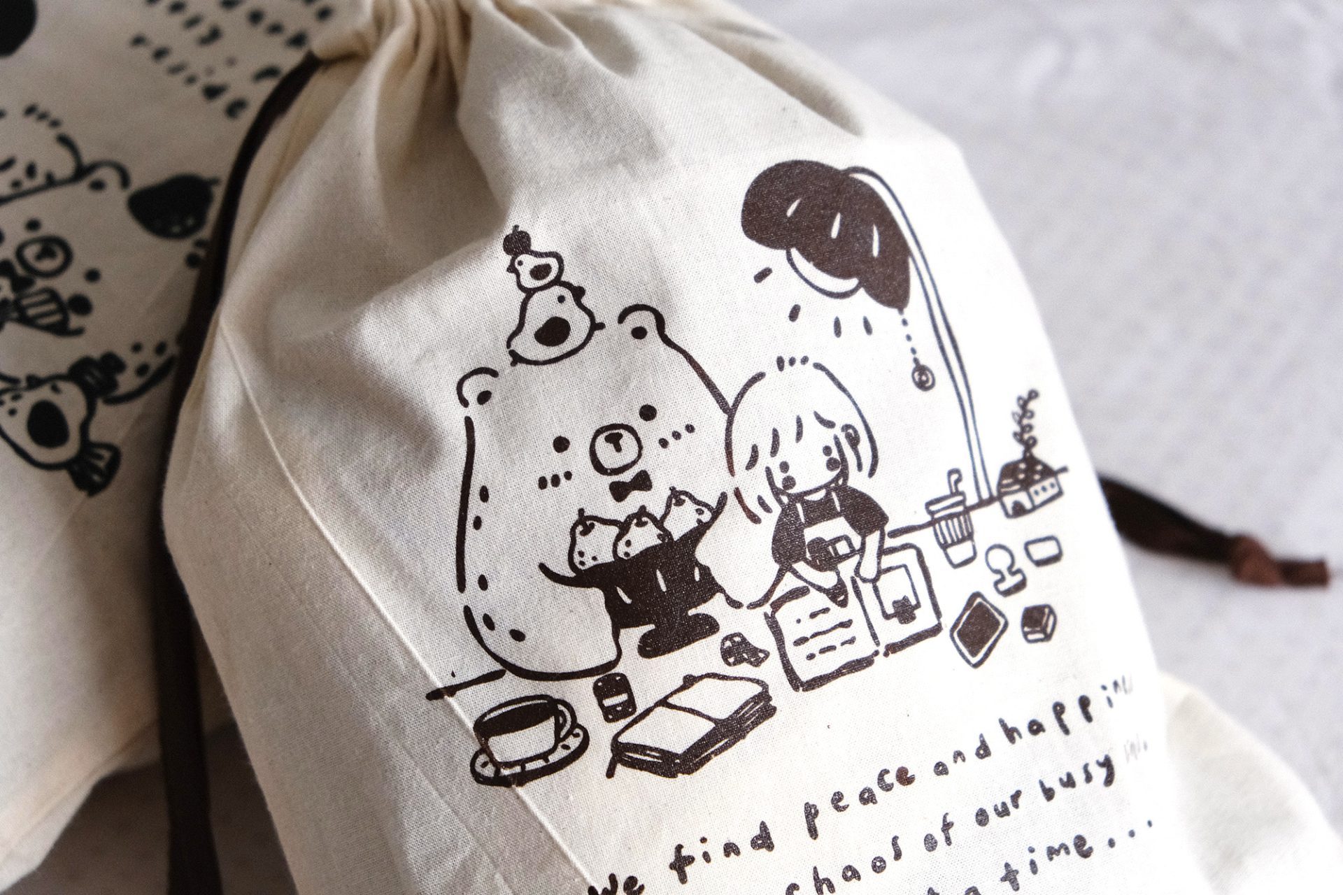 Angled view of an Eileen Tai brown drawstring pouch with character illustration and drawstring closure.