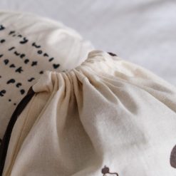 Front view of an Eileen Tai drawstring pouch with illustrated characters and handwritten quote, featuring brown drawstrings.