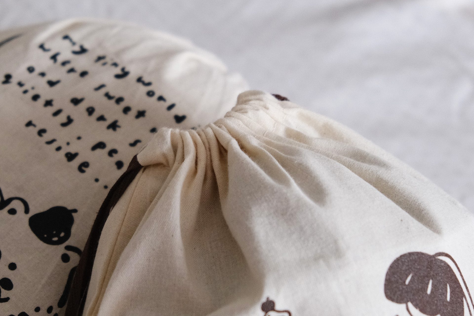 Front view of an Eileen Tai drawstring pouch with illustrated characters and handwritten quote, featuring brown drawstrings.