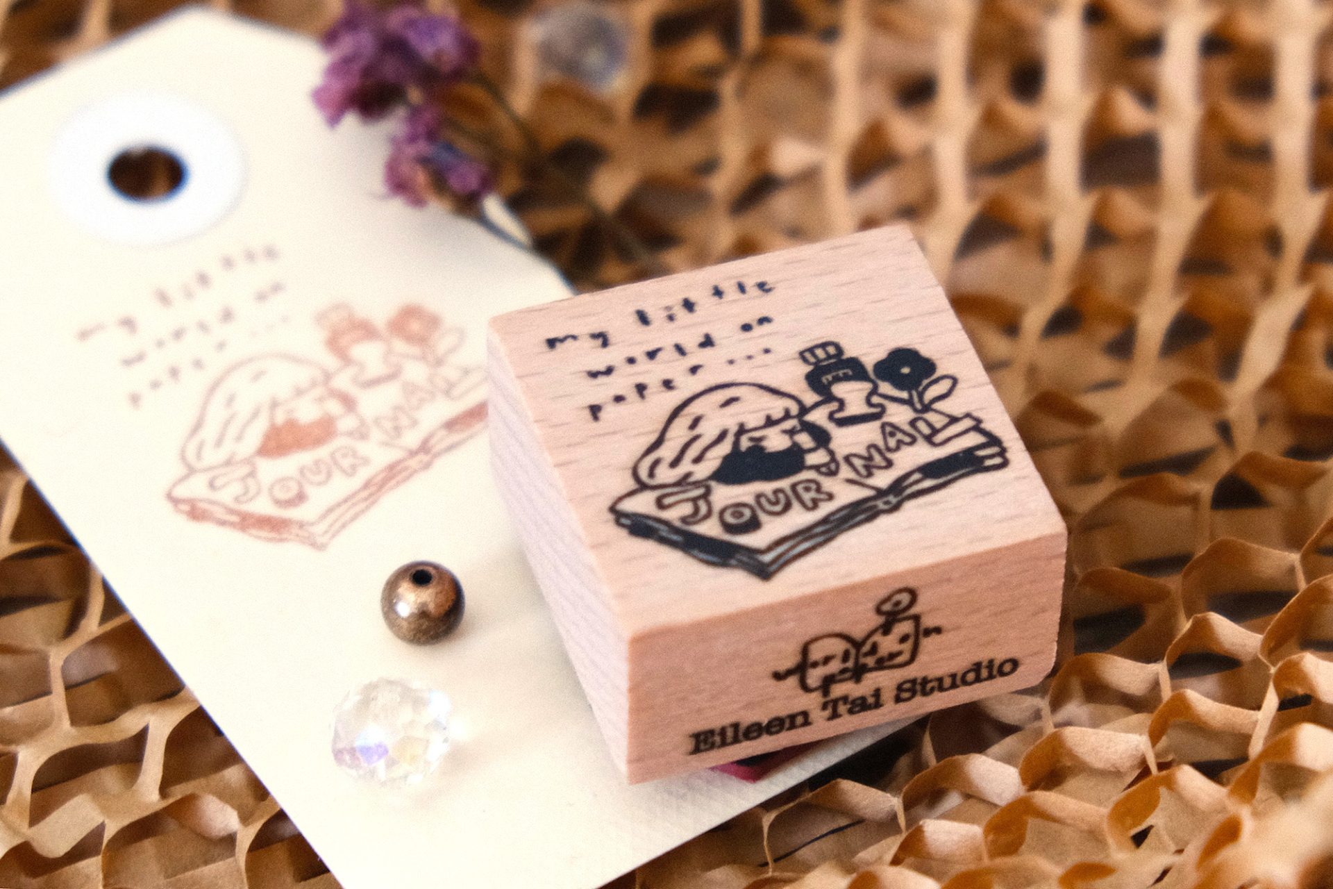 Styled image of an Eileen Tai journal girl rubber stamp with a stamped paper tag.
