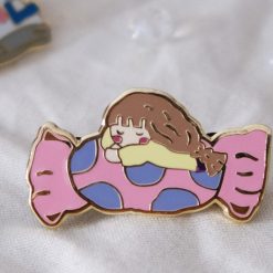 Close-up styled photo of an Eileen Tai sweet like candy enamel pin on a soft fabric background.