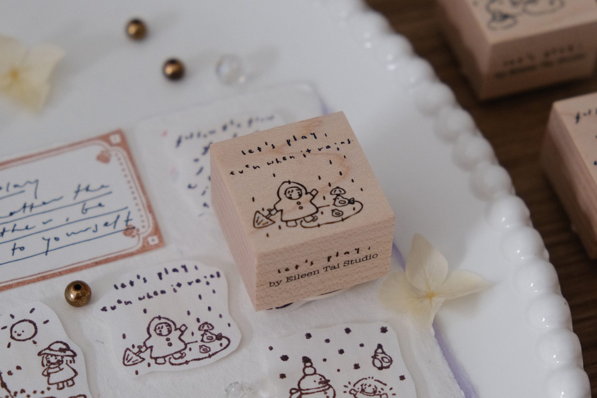 Let’s Play wooden stamp showing a child playing in the rain with the phrase “let’s play even when it rains”.