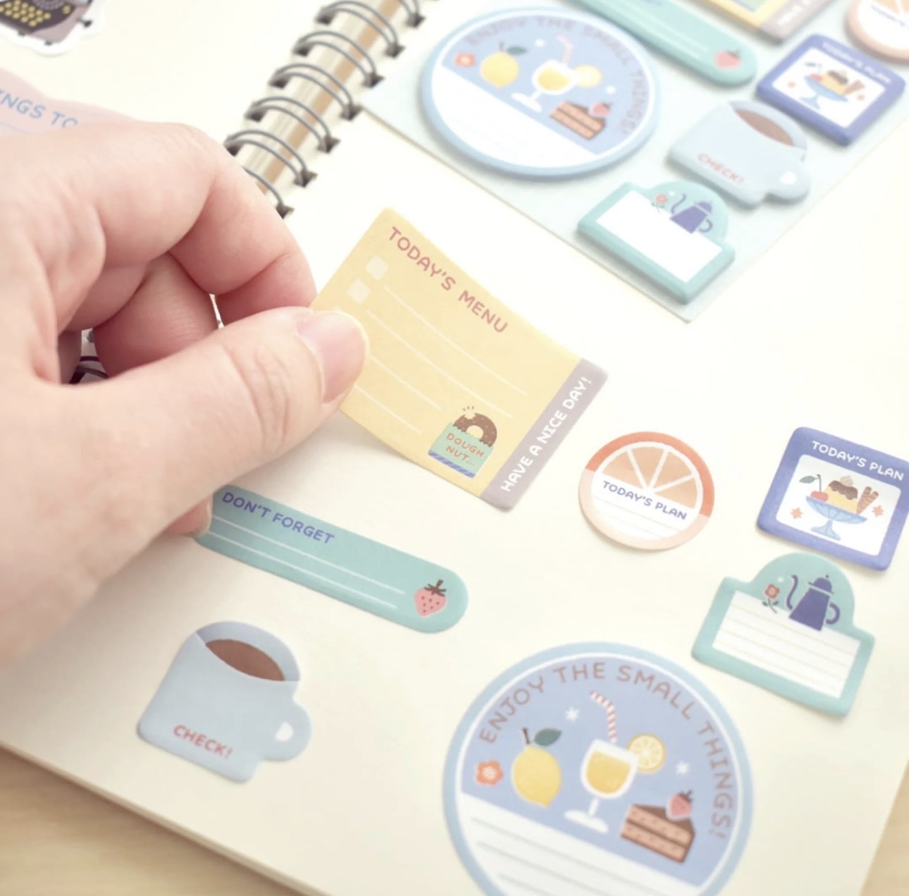 Close-up of a hand holding a mini stationery sticky note from the Eric Small Things set, with additional sticky notes visible in the background on a wood tabletop.