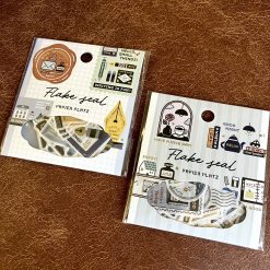 Papier Platz Eric Small Things writing tools washi sticker pack photographed on a brown surface, showing packaging and sticker flakes.